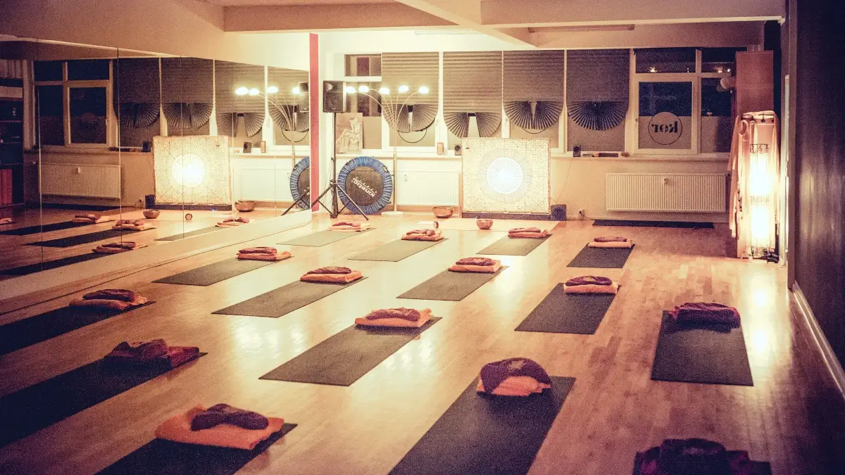 Innenansicht eines Yoga-Studios mit mehreren Matten und Kissen, warm beleuchtet, ruhige und entspannende Atmosphäre für Yoga- oder Meditationskurse